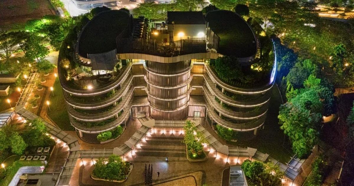 Aerial view of a sustainable hospitality building surrounded by green roofs, gardens, and night lighting.